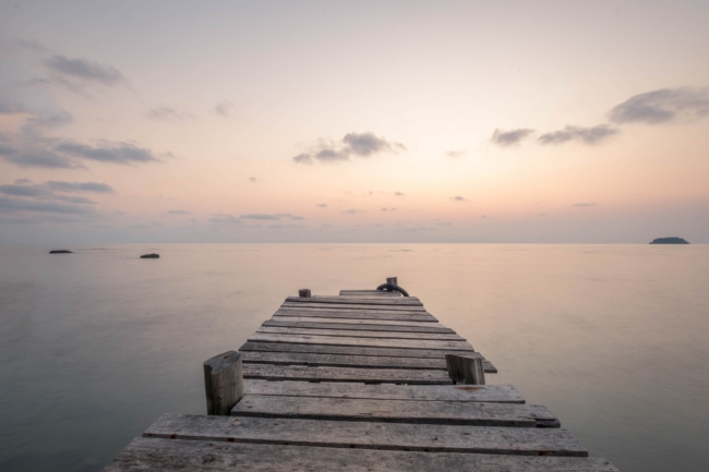 An empty wooden dock extending into calm water, suggesting reflection, transition, and inner transformation.